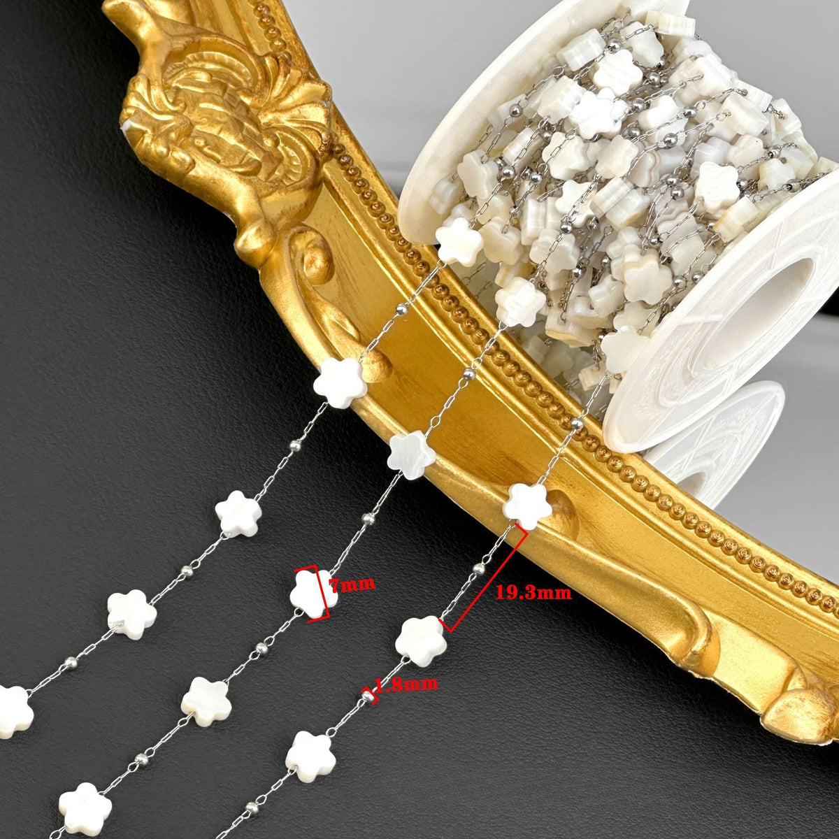 Spool of white flower-bead station chain draped over ornate gold frame with size measurement labels.