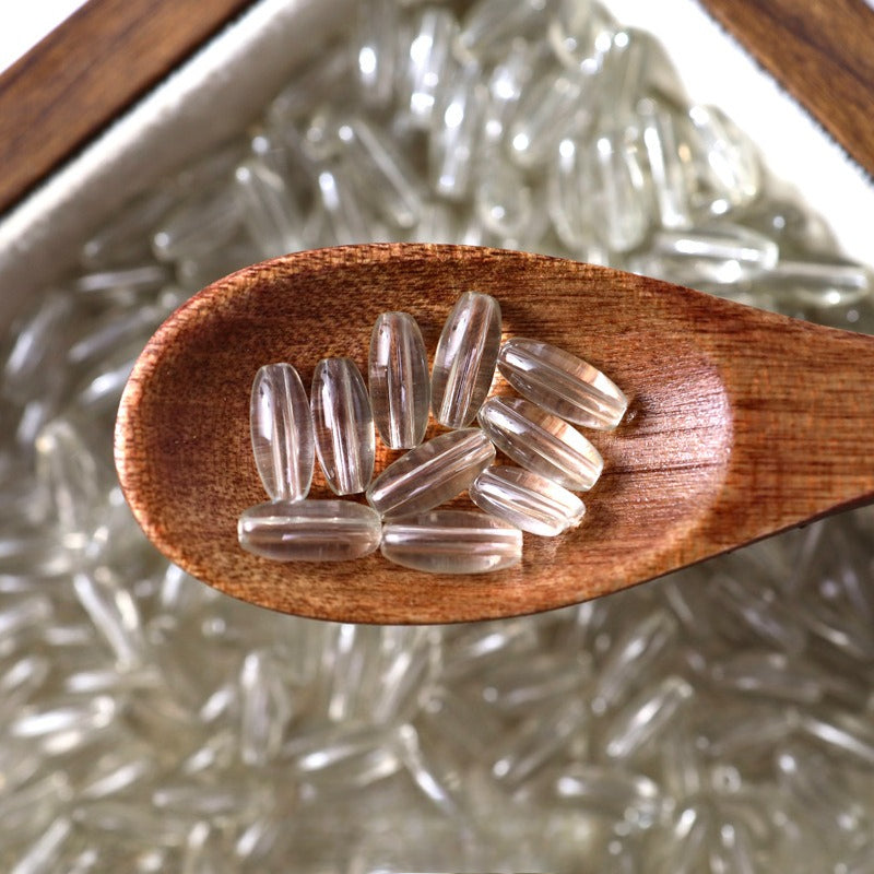 Clear translucent 4x9mm glazed glass long rice beads in a wooden spoon