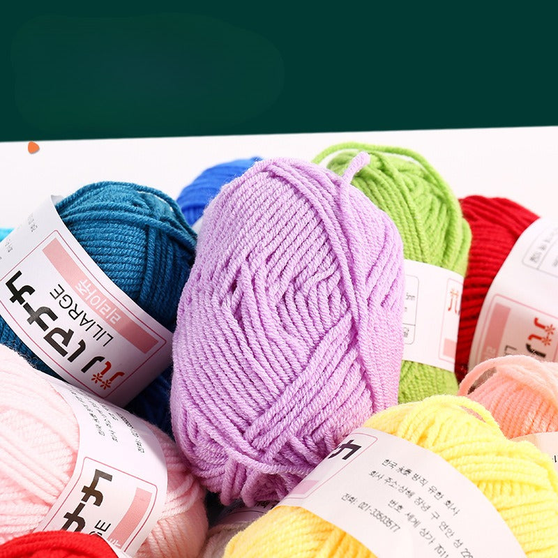 A close-up arrangement of colorful yarn skeins with white labels, including blue, purple, green, red, pink, yellow, and orange, photographed on a white surface against a dark green background.