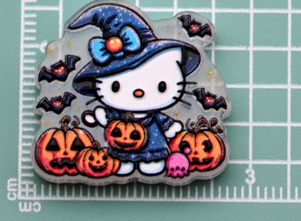 Hello Kitty blue witch acrylic charm with pumpkins, bats, and pink skull on green cutting mat