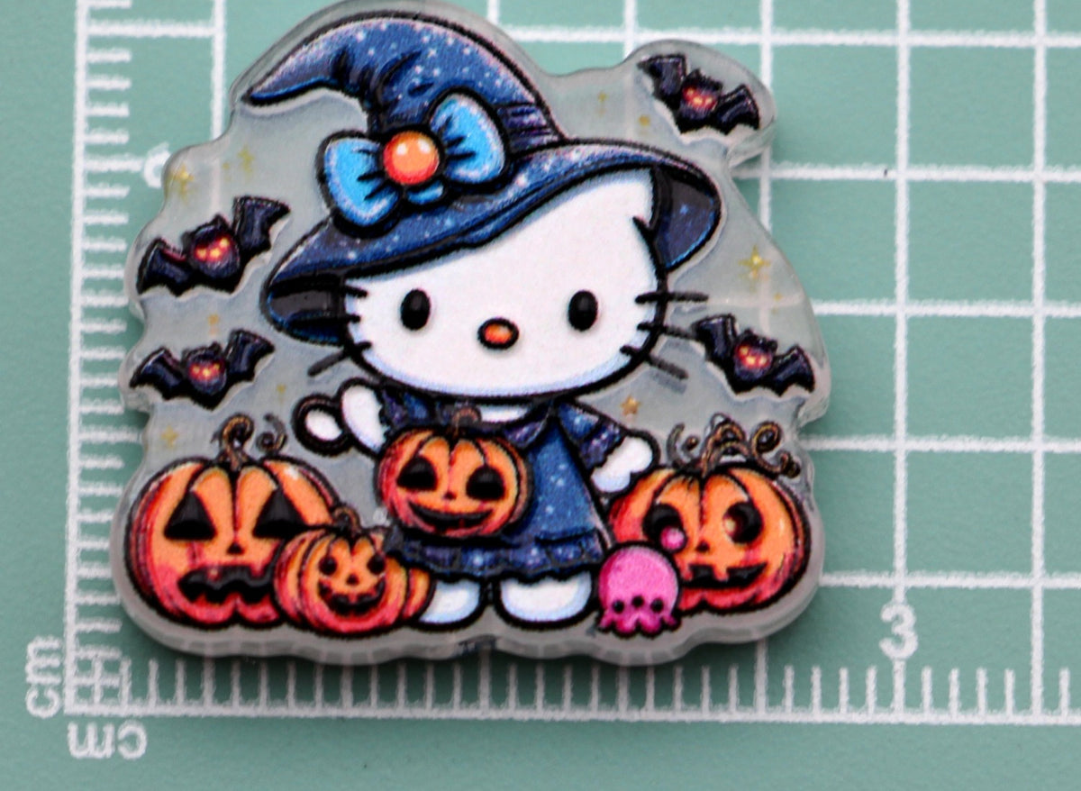 Hello Kitty blue witch acrylic charm with pumpkins, bats, and pink skull on green cutting mat