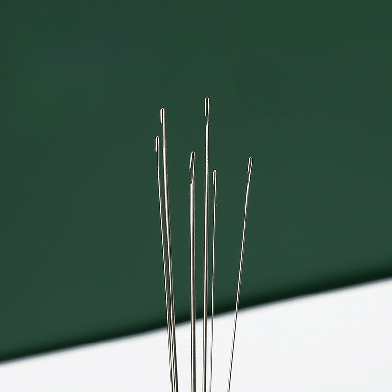 Five slim metallic hook needles standing upright against a dark green background and white surface.