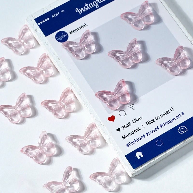 Translucent pink butterfly-shaped glass beads on a white surface beside a printed card