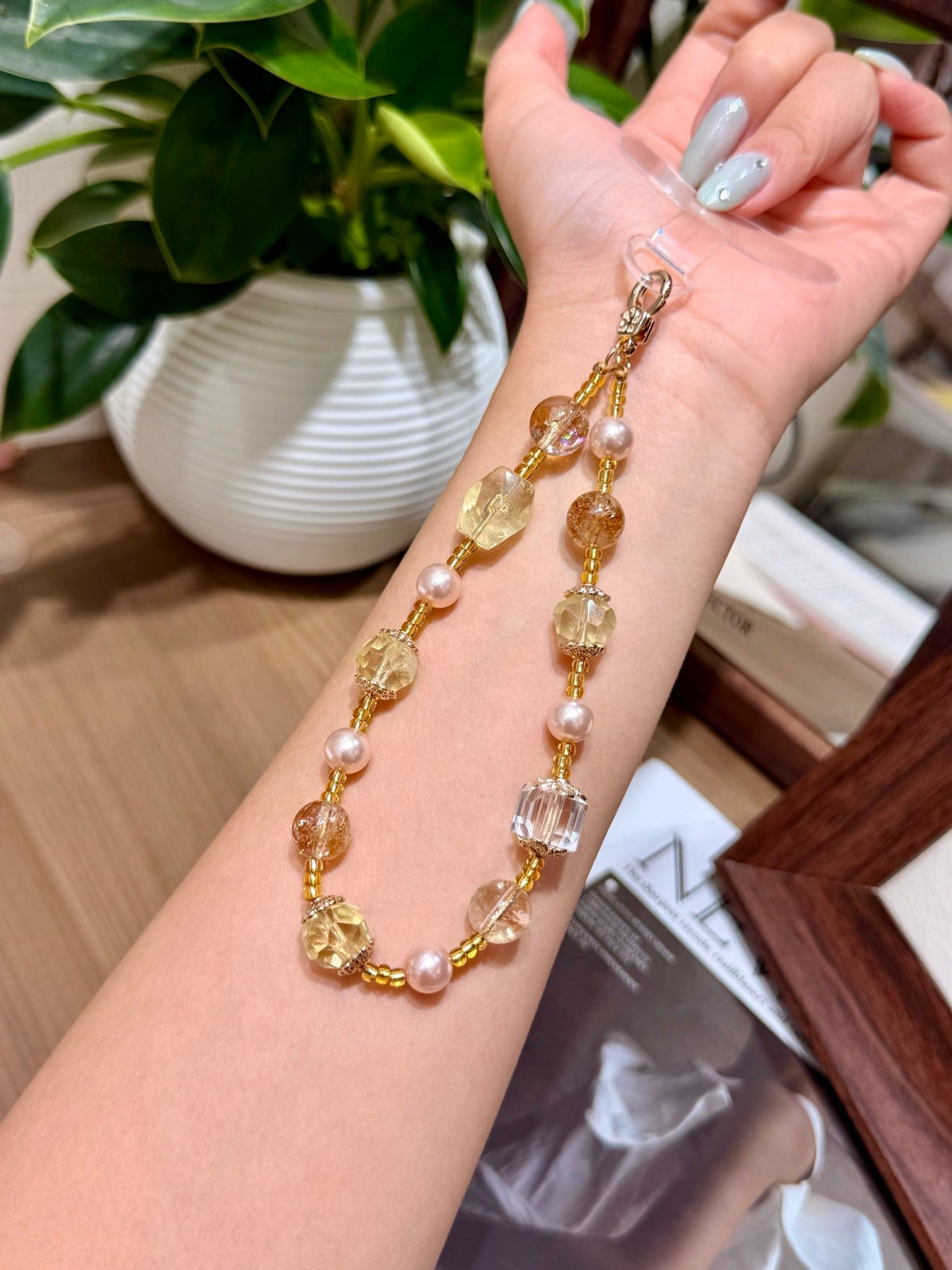 Wrist wearing a gold beaded phone charm with citrine crystals, shell pearls and clear glass cubes