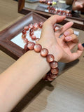 Pink lepidolite bead bracelet worn on a wrist, with more beads on a wooden tray