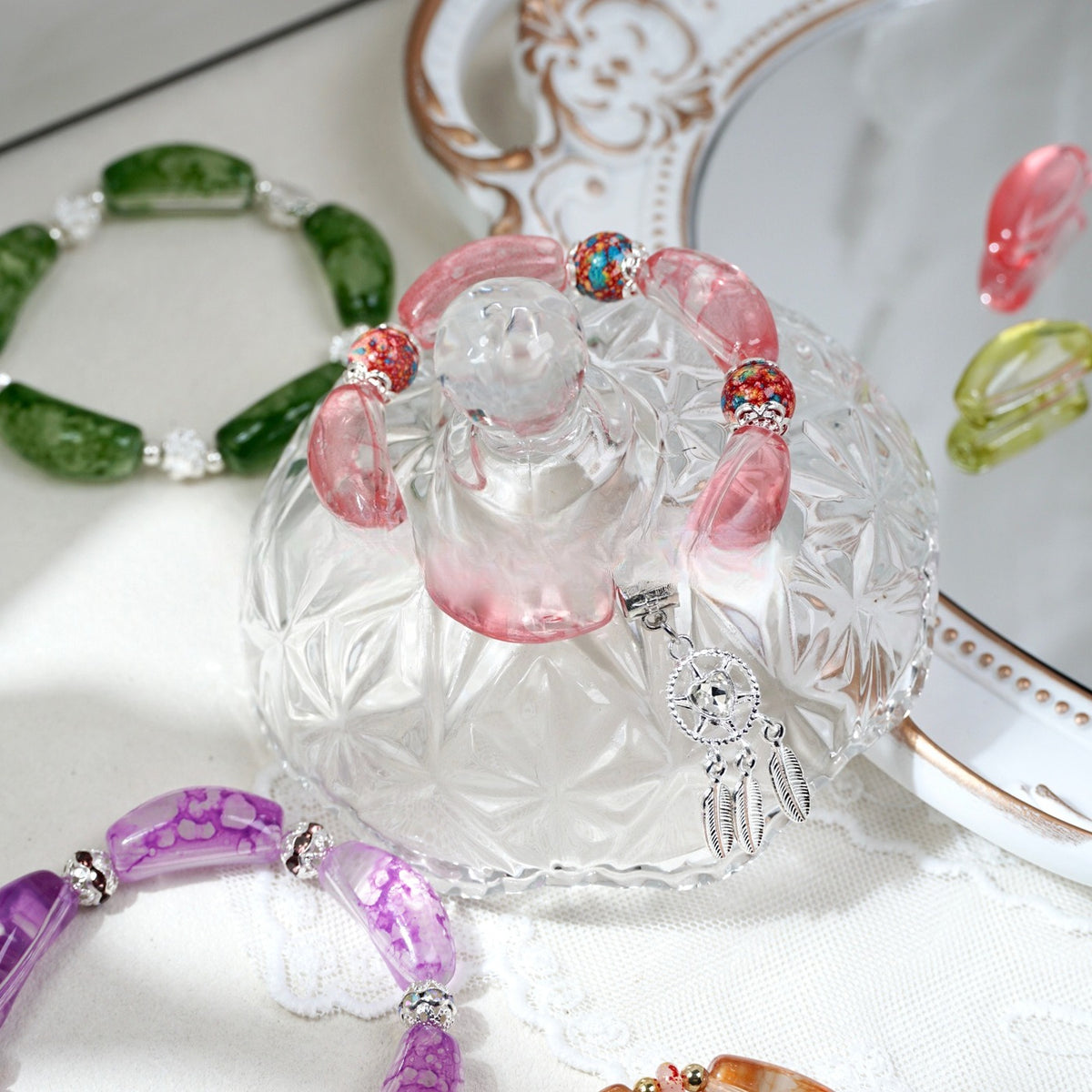 Pink translucent curved glass tube bead bracelet with colorful accent beads and a silver dreamcatcher charm on a glass stand