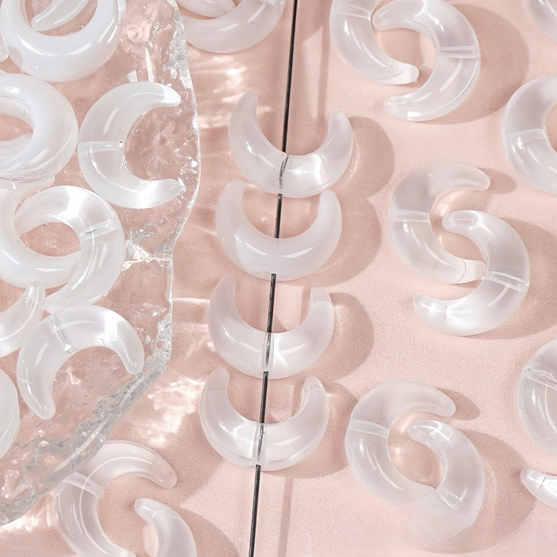 Clear glazed glass crescent moon beads, some threaded on a thin black string and others on a textured clear surface