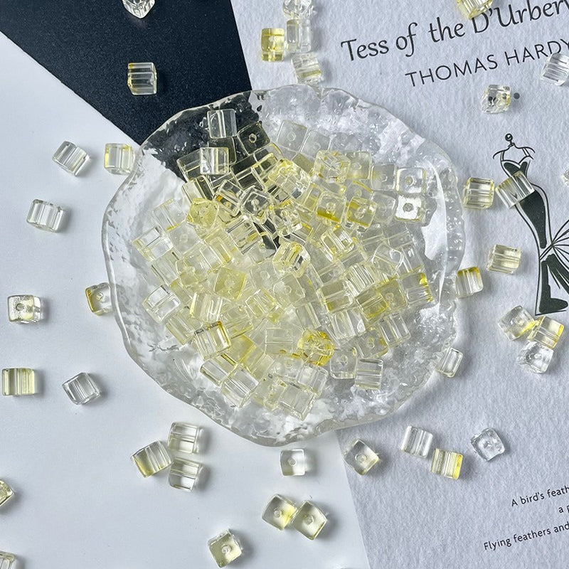 Clear cube glass beads with pale yellow centers in glass dish, scattered