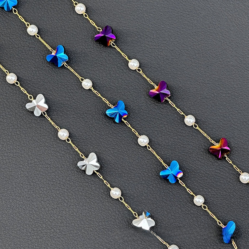 Three gold chain strands with white pearl beads and blue, purple, silver butterfly charms on dark gray
