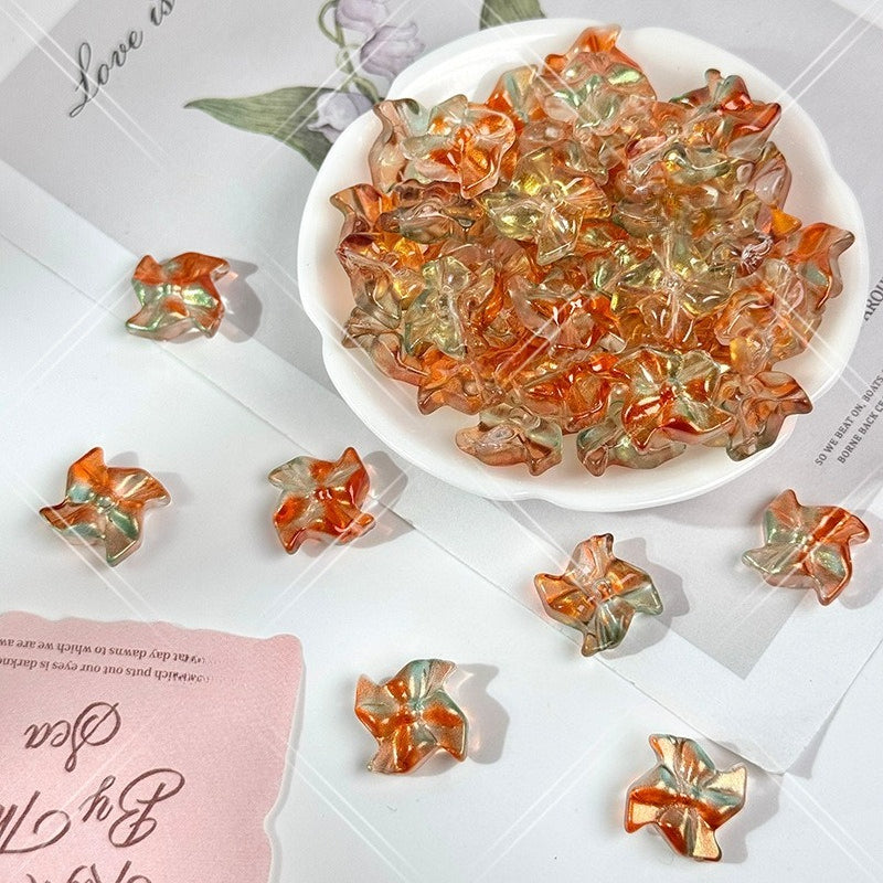 Iridescent 20mm carved glass windmill beads in orange, peach and pale green tones in a bowl on white paper