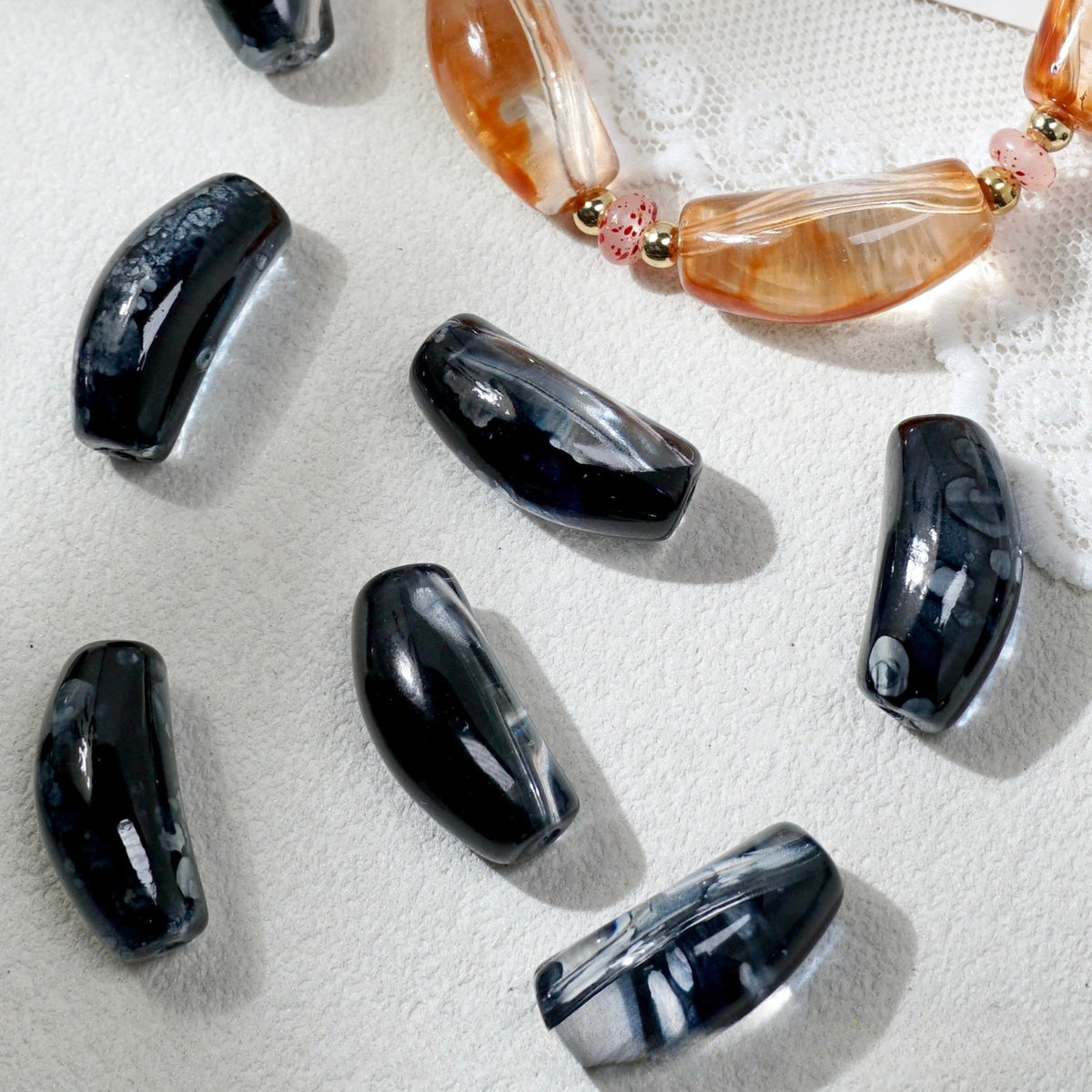 Glossy black marbled curved glass tube beads scattered on white textured fabric