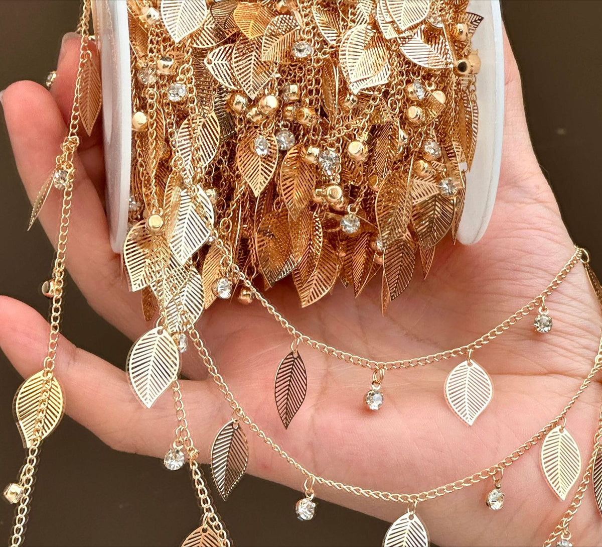 Hand holding large spool of gold leaf rhinestone fringe chain garlands
