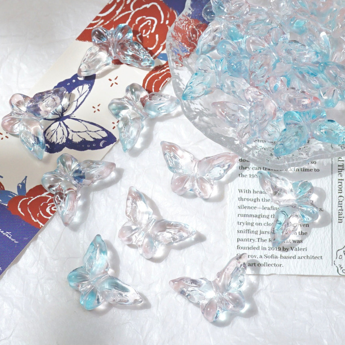 Clear butterfly-shaped glass beads with light blue and pink iridescent reflections scattered on white