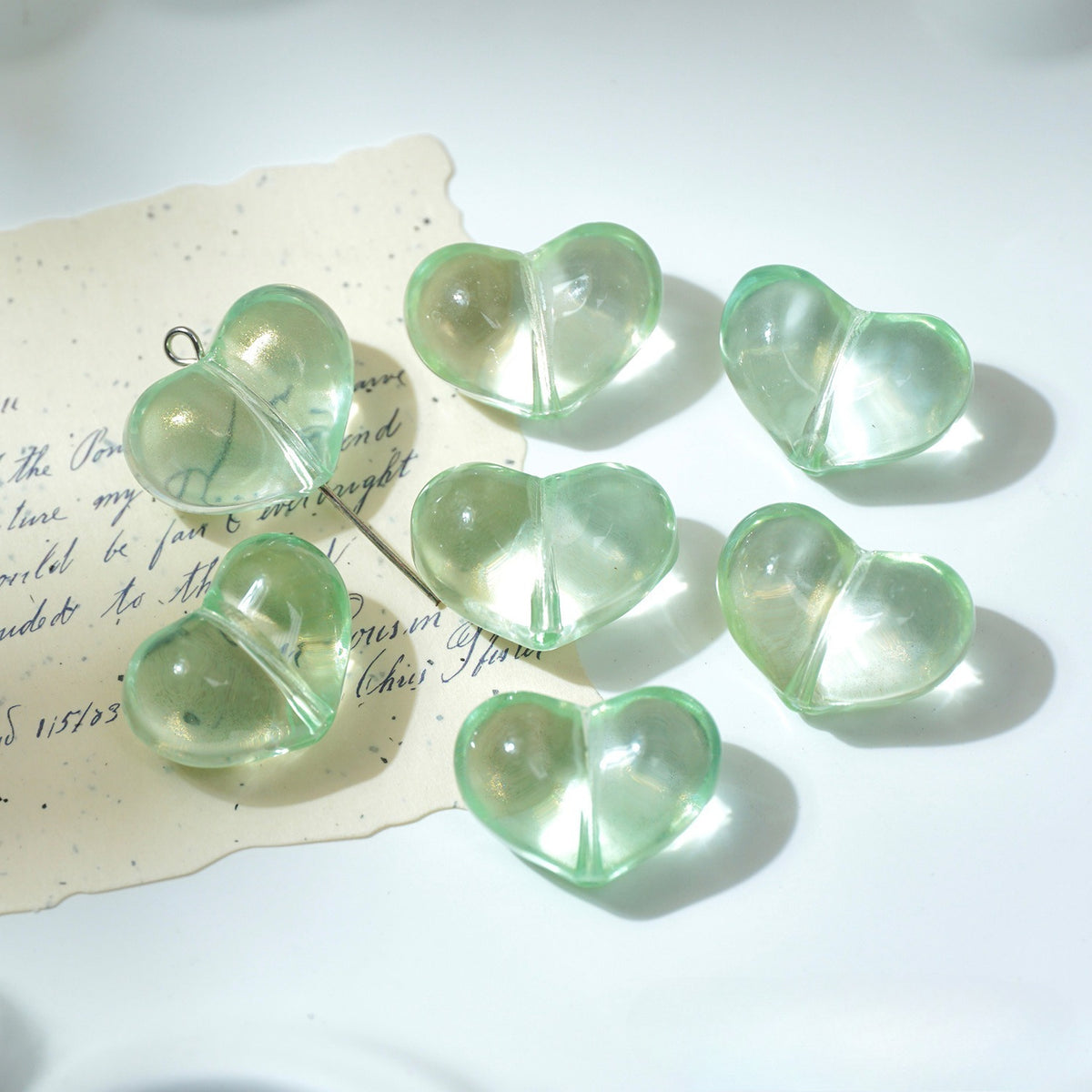 Six translucent light green heart-shaped glass beads with metal loops on white