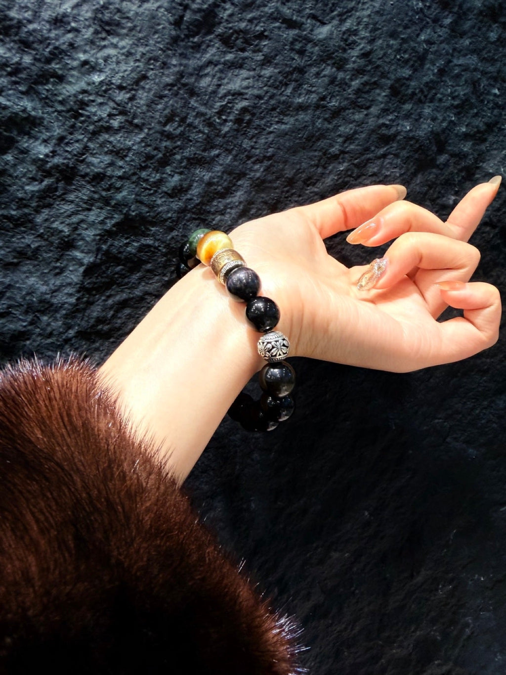 Close-up of wrist wearing black obsidian beaded bracelet with gold mantra beads