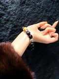 Close-up of wrist wearing black obsidian beaded bracelet with gold mantra beads