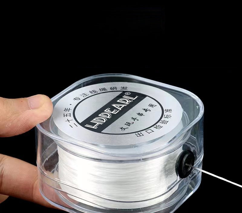 Hand holding a clear plastic spool of white elastic beading cord with black knob on solid black background