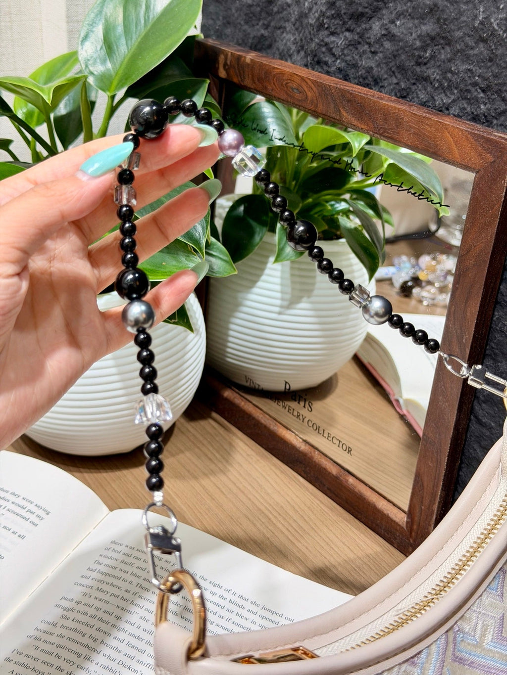 Hand holding black beaded bag charm with silver and clear crystal beads, attached to a cream bag.