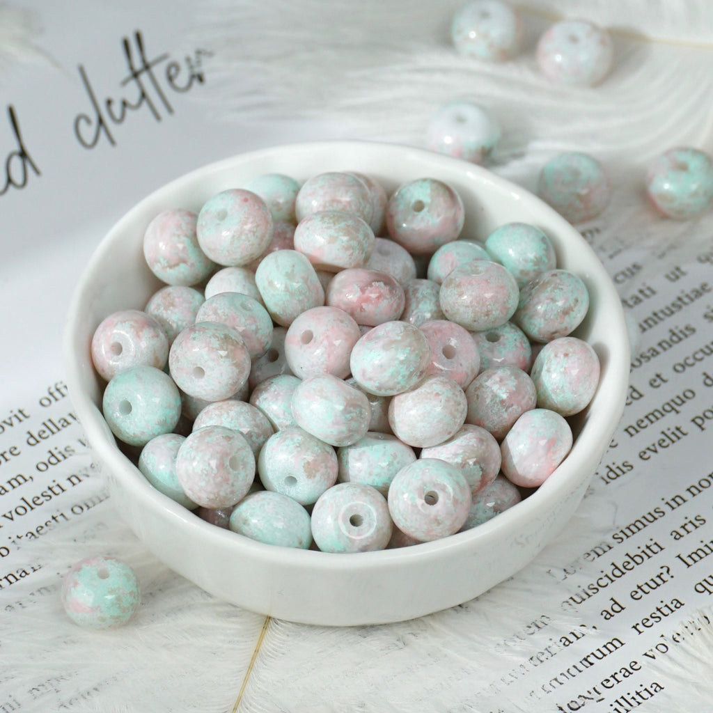 Round marbled beads in pastel pink, mint green and white in a small white porcelain bowl on printed paper