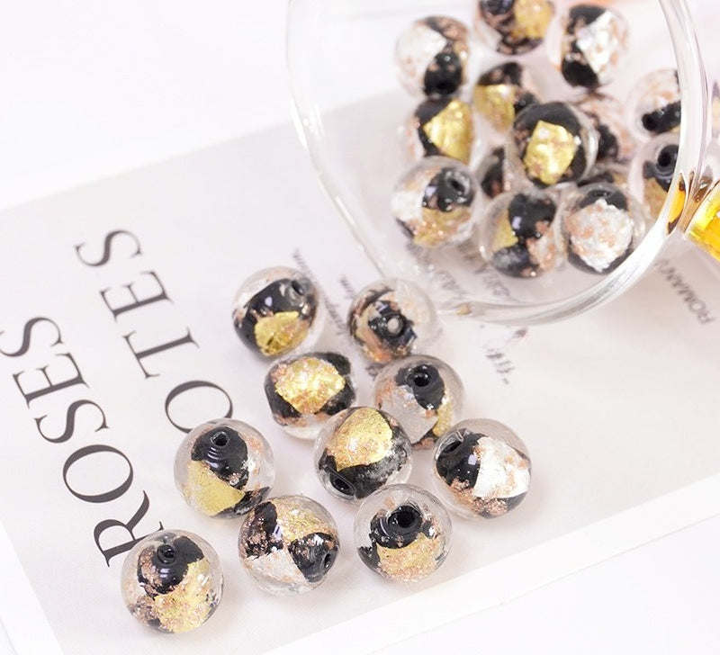 Clear round beads with black and gold foil accents, shown spilling from a glass jar onto a white printed card.