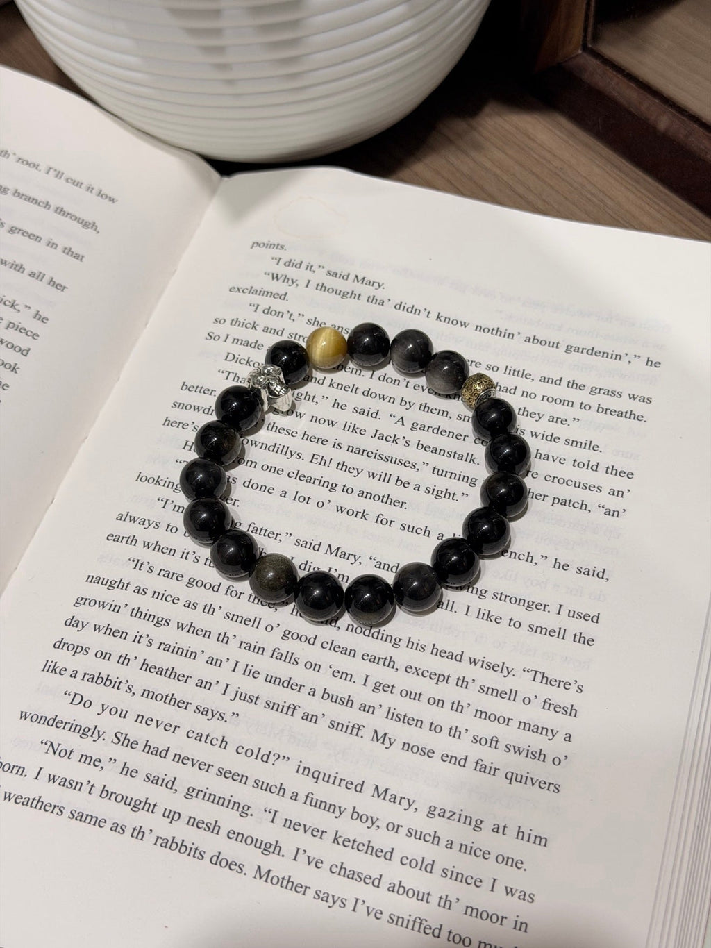 Black beaded bracelet with silver charm and gold accent beads resting on open book