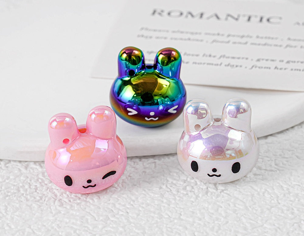 Three glossy bunny-shaped acrylic pendant charms in pastel colors on white surface
