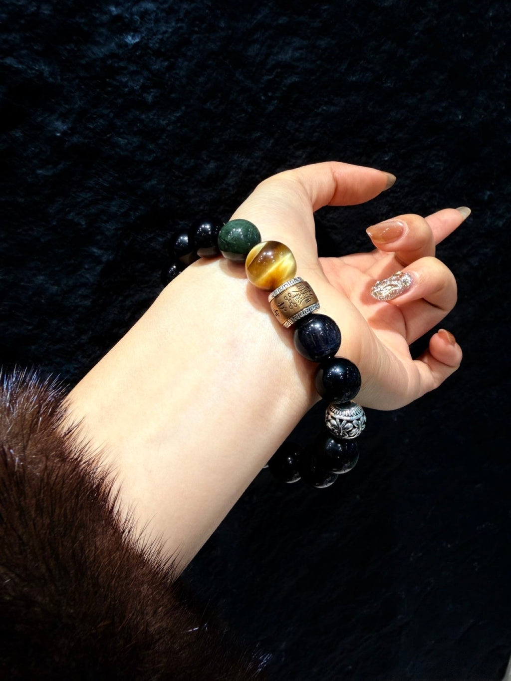 Close-up of wrist wearing black beaded bracelet against dark textured background