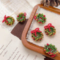 Beaded Christmas wreath ornaments with red bows in red, green, and gold seed beads on a wooden tray