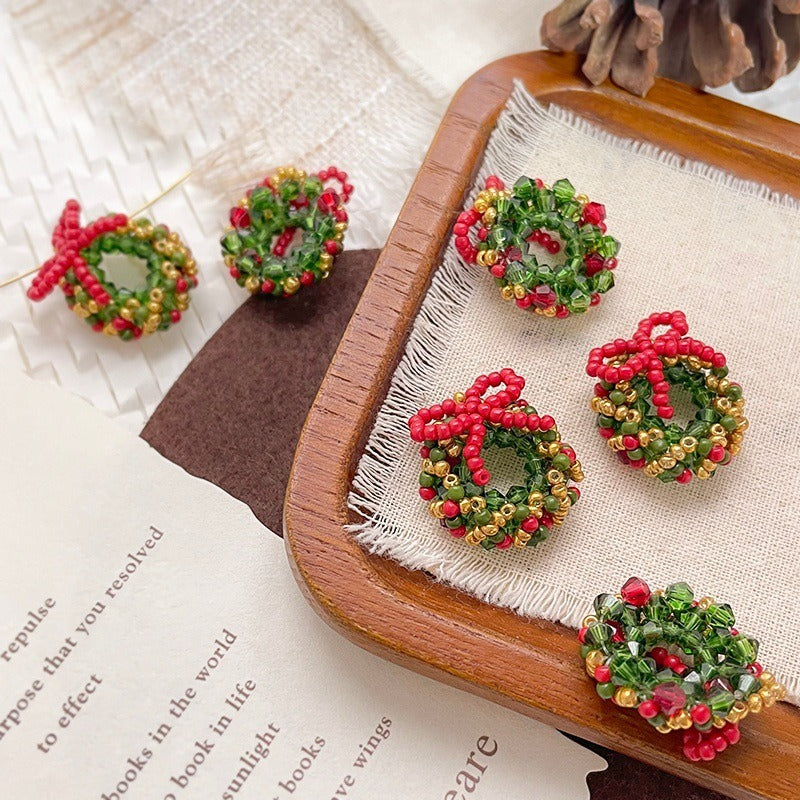Beaded Christmas wreath ornaments with red bows in red, green, and gold seed beads on a wooden tray
