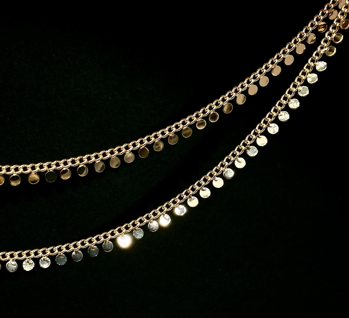 Close-up of gold disc chain with small round metallic discs on a black background.