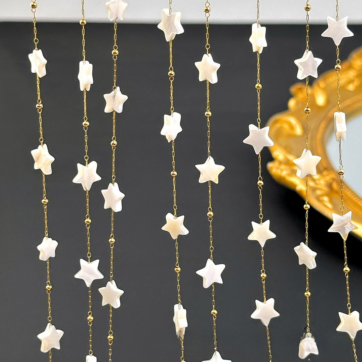 White star-shaped beads on hanging gold chains against a dark background with a gold ornate mirror