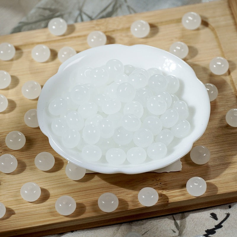 Translucent white imitation jade glass beads in a scalloped dish on a wooden board