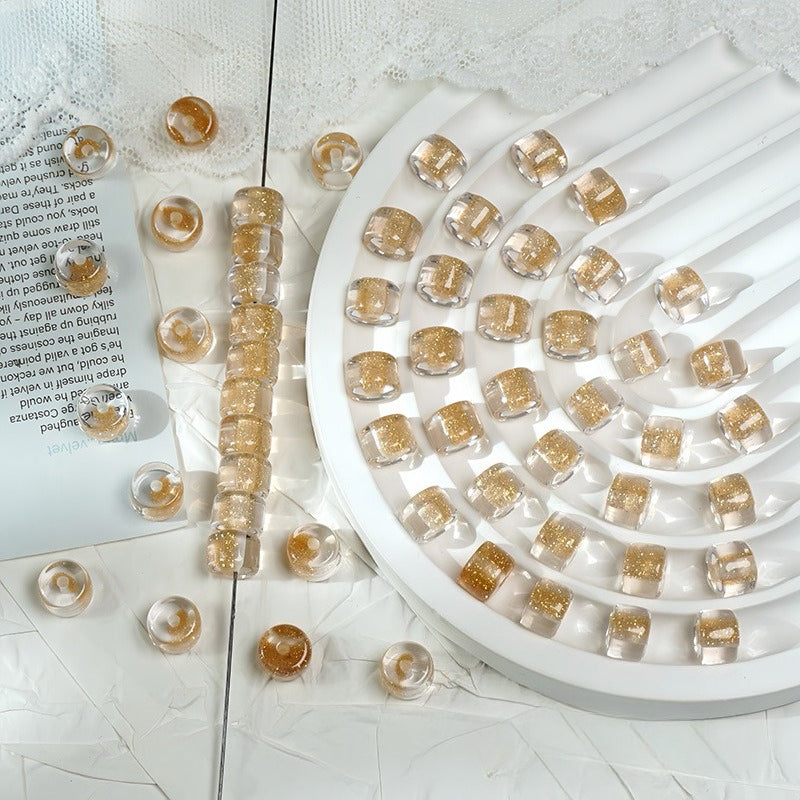 Champagne gold glitter barrel beads on a white spiral tray with loose beads on a printed card and white surface