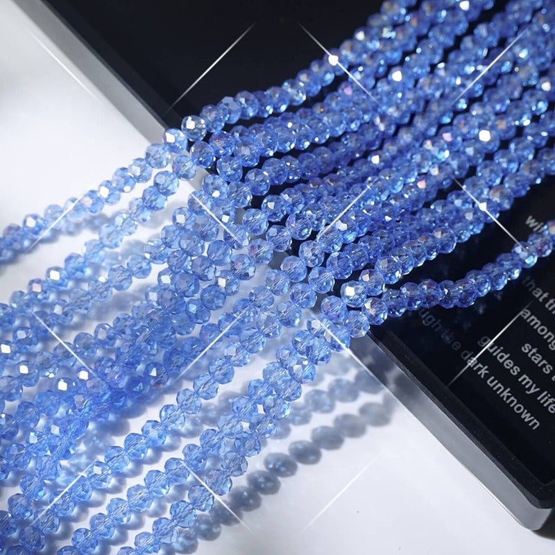 Light blue faceted crystal glass wheel bead strands arranged diagonally on white surface