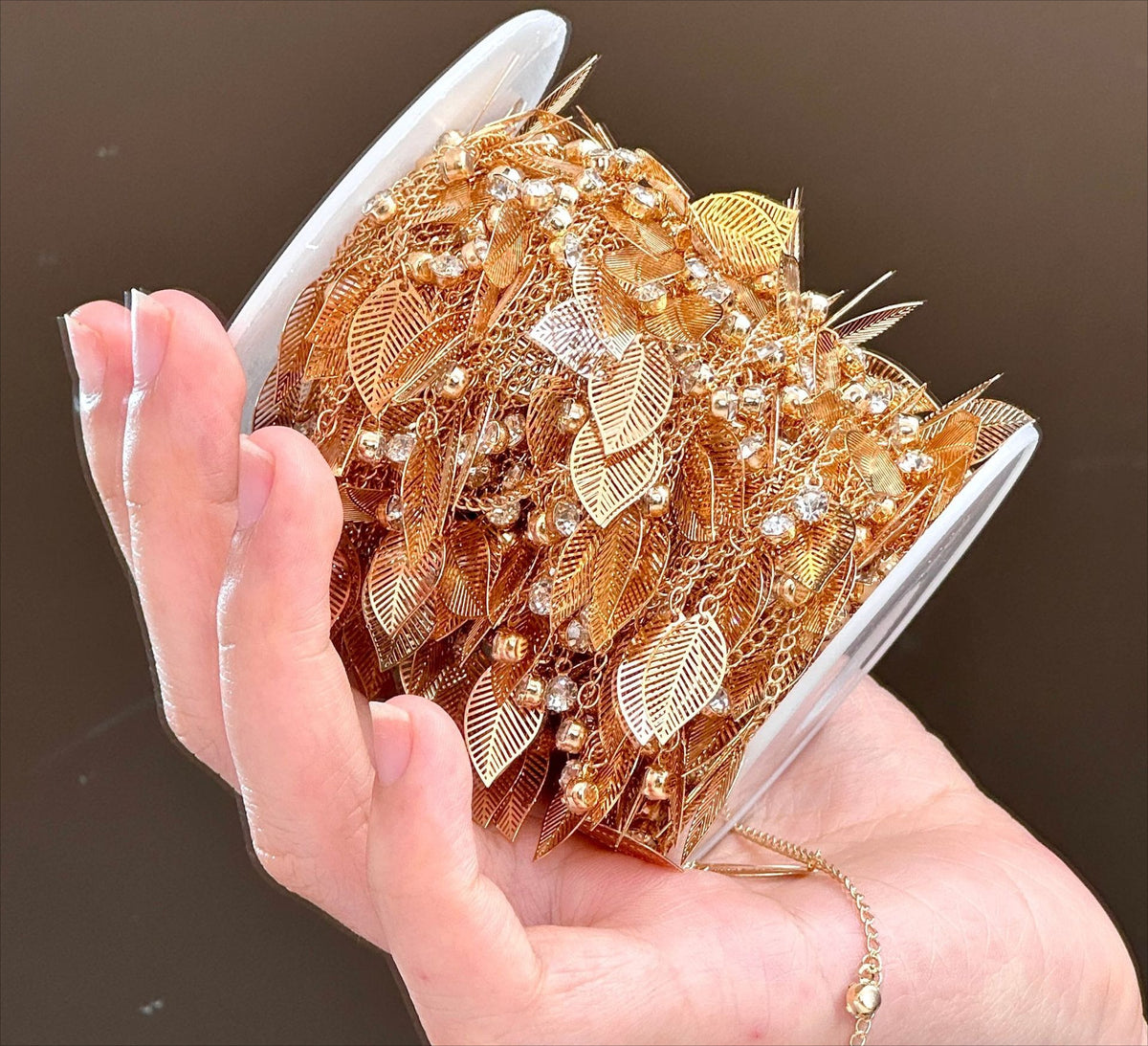 Hand holding clear spool of gold leaf rhinestone fringe chain