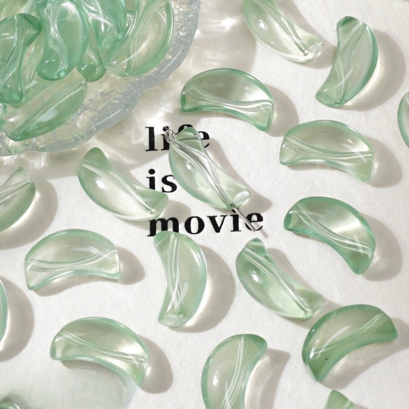 Pale green translucent crescent glass beads on white with 'life is movie' text and a dish