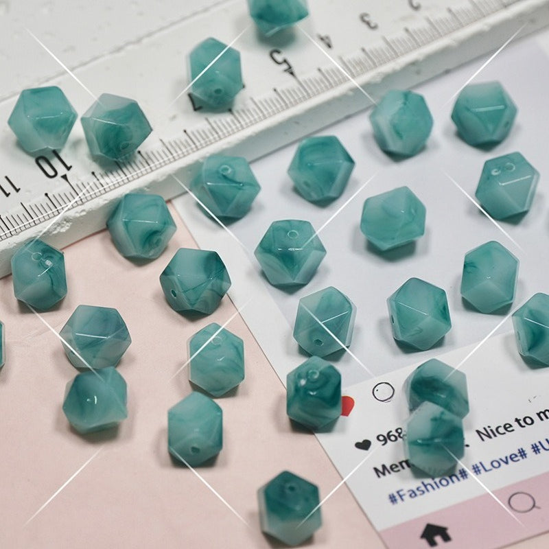 Faceted teal beads scattered on a white and pale pink surface with a ruler