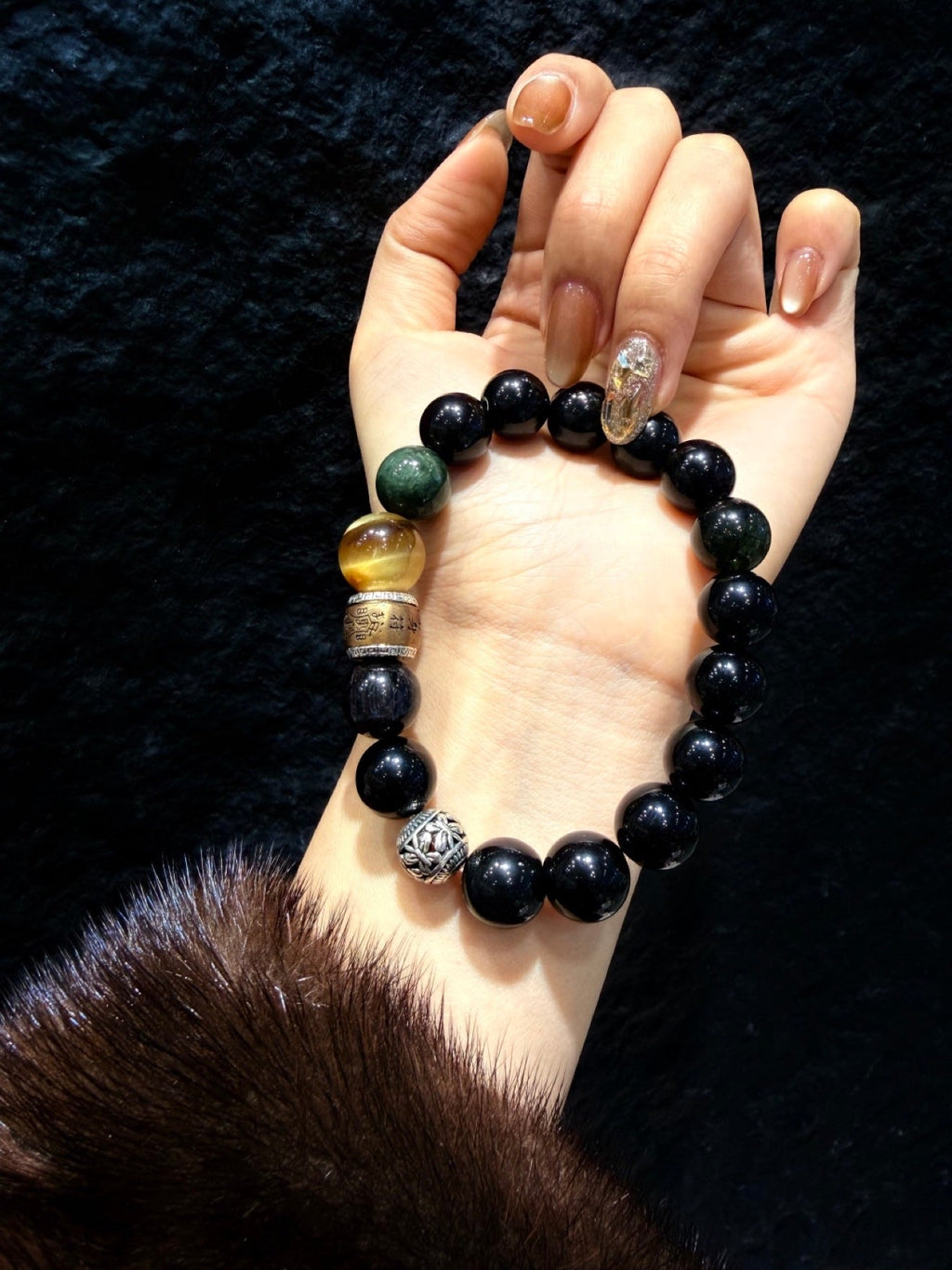 Wrist wearing beaded bracelet with glossy black beads and gold accent beads
