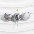 Three baroque freshwater pearls with iridescent blue, purple, and gold marbling on a white background.