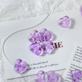 Translucent light purple heart-shaped glass beads on a white card with matching purple beads nearby