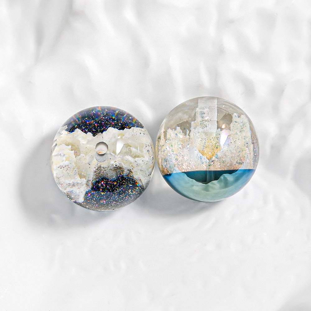 Two clear round resin beads with split design: white cloud glitter, blue ocean wave, and gold foil on white background.