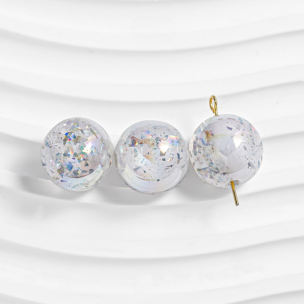 Three transparent round beads with iridescent glitter on white; right bead has gold loop and pin