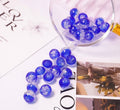 Close-up of blue two-tone glow-in-the-dark glass beads pouring from a glass cup onto a printed card