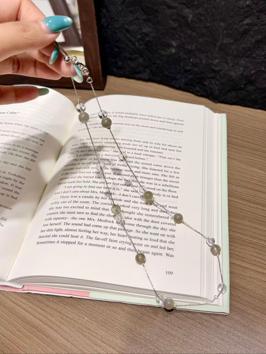 Hand holding misty moon beaded necklace over open book