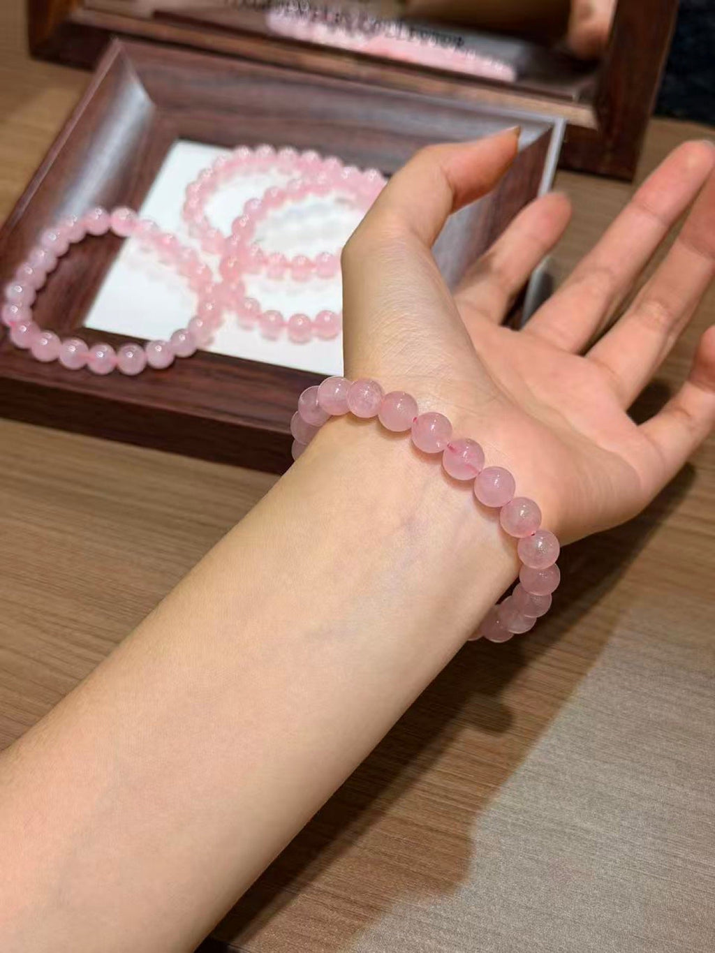 Wrist wearing pink translucent beaded bracelet, matching bracelets on wooden tray behind