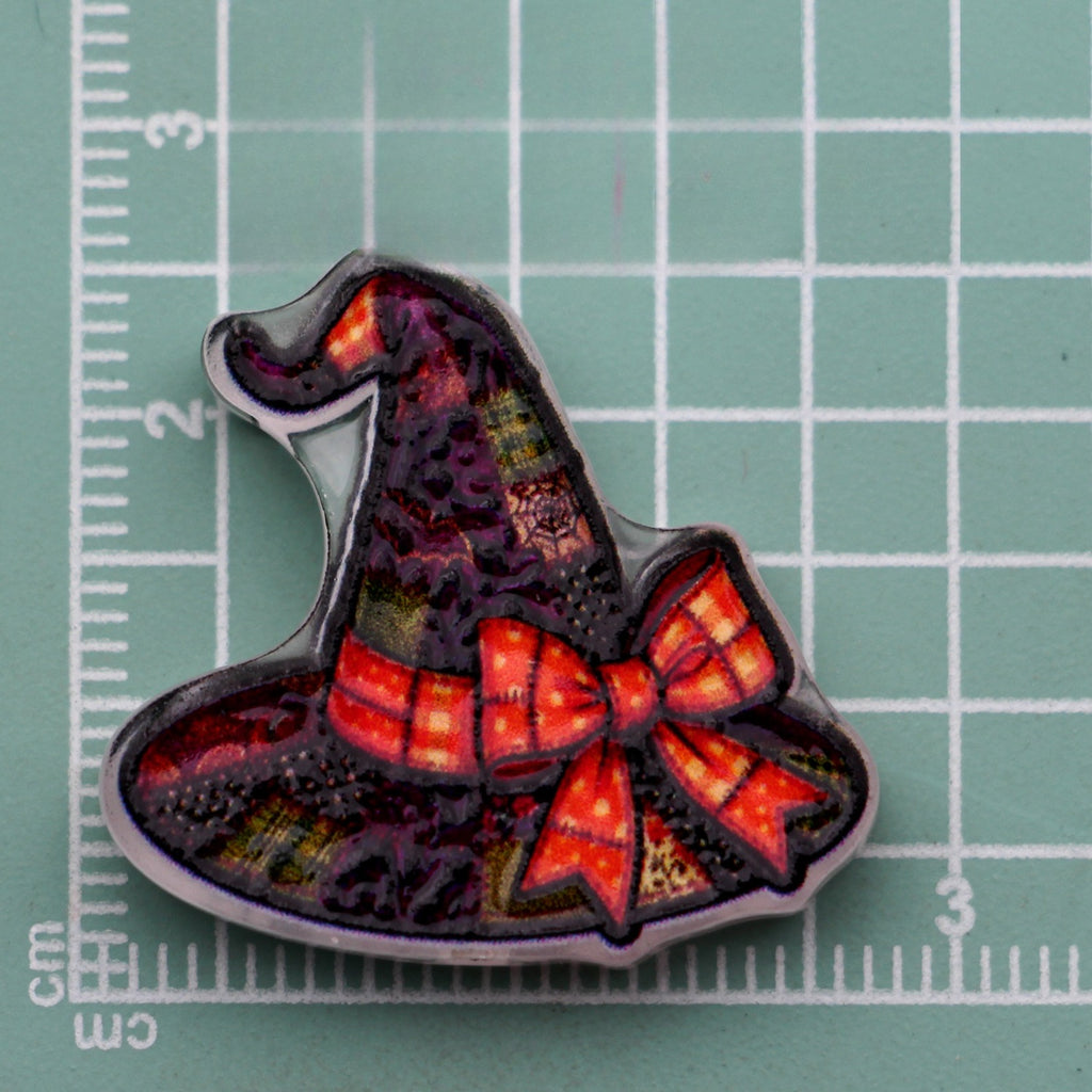 Halloween acrylic bead shaped as a witch hat with a red-orange plaid bow on a green cutting mat