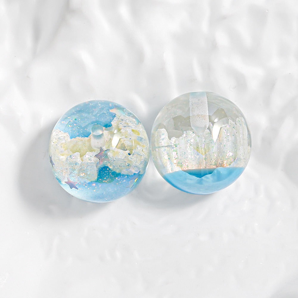 Two round transparent resin cabochons with blue glitter and white castle-like details, shown on a white textured background.