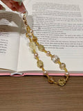 Hand holding a gold beaded phone charm with citrine crystals, shell pearls and clear glass cubes over an open book