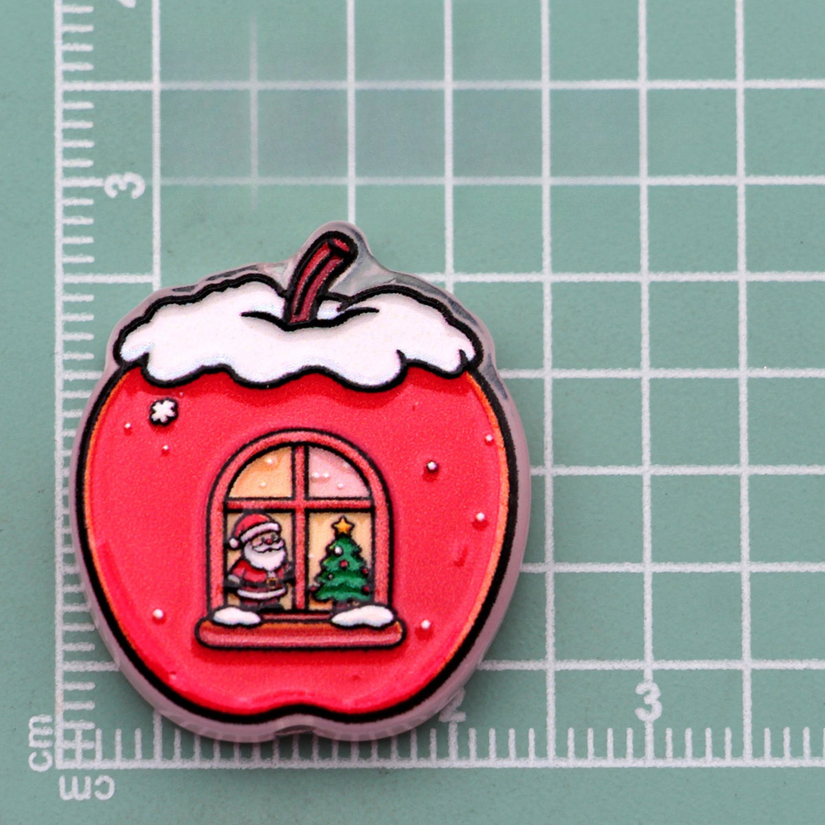 Apple house acrylic charm with red apple, snow cap, and Santa in window on green cutting mat