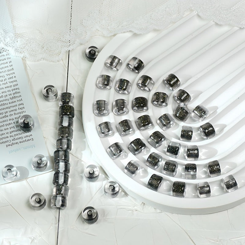 Dark grey glitter barrel beads on a white circular tray with lace fabric and printed paper props